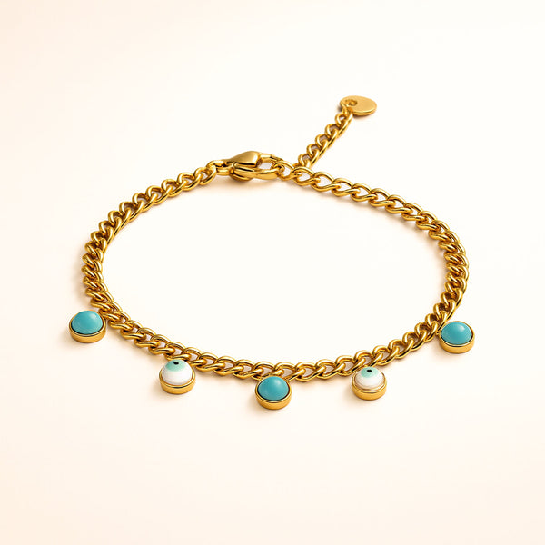 Gold chain bracelet with turquoise and pearl charms on a beige background