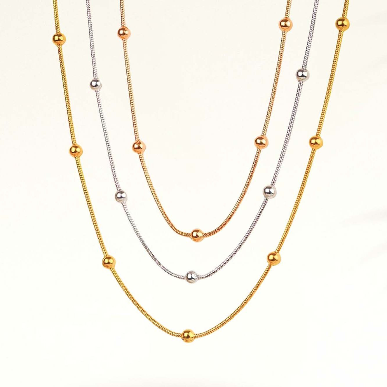 Two gold necklaces with small beads on a white background